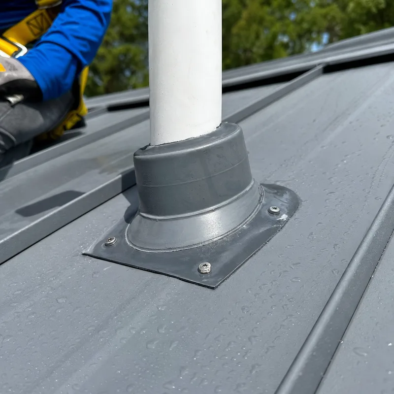 Metal roof flashing at a plumbing vent beside standing seam panels